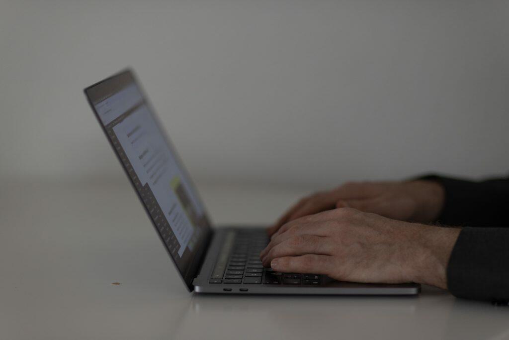 Hænder, der strategisk skriver på et bærbart tastatur, set fra siden med en sløret baggrund, og skaber det perfekte brandimage.