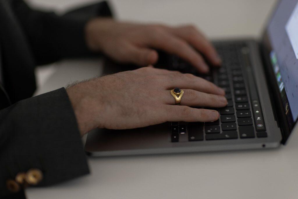 Person i mørk blazer, der skriver på et bærbart tastatur, fokuseret på at lave en brandingstrategi. De bærer en guldring med en mørk sten på deres højre hånd, hvilket tilføjer sofistikeret billedet.