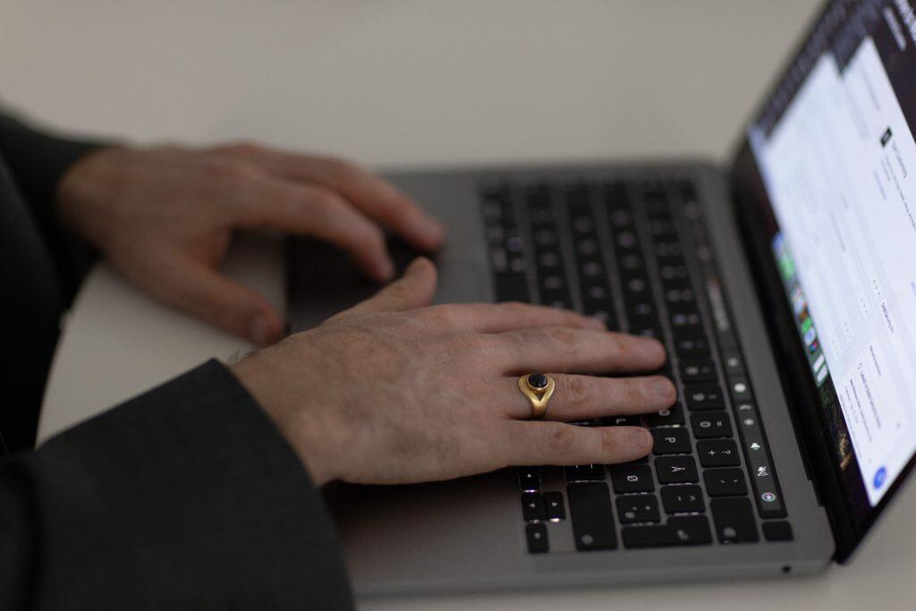 En person skriver strategisk på en bærbar computer, og deres guldring skinner, mens de laver et image til branding.