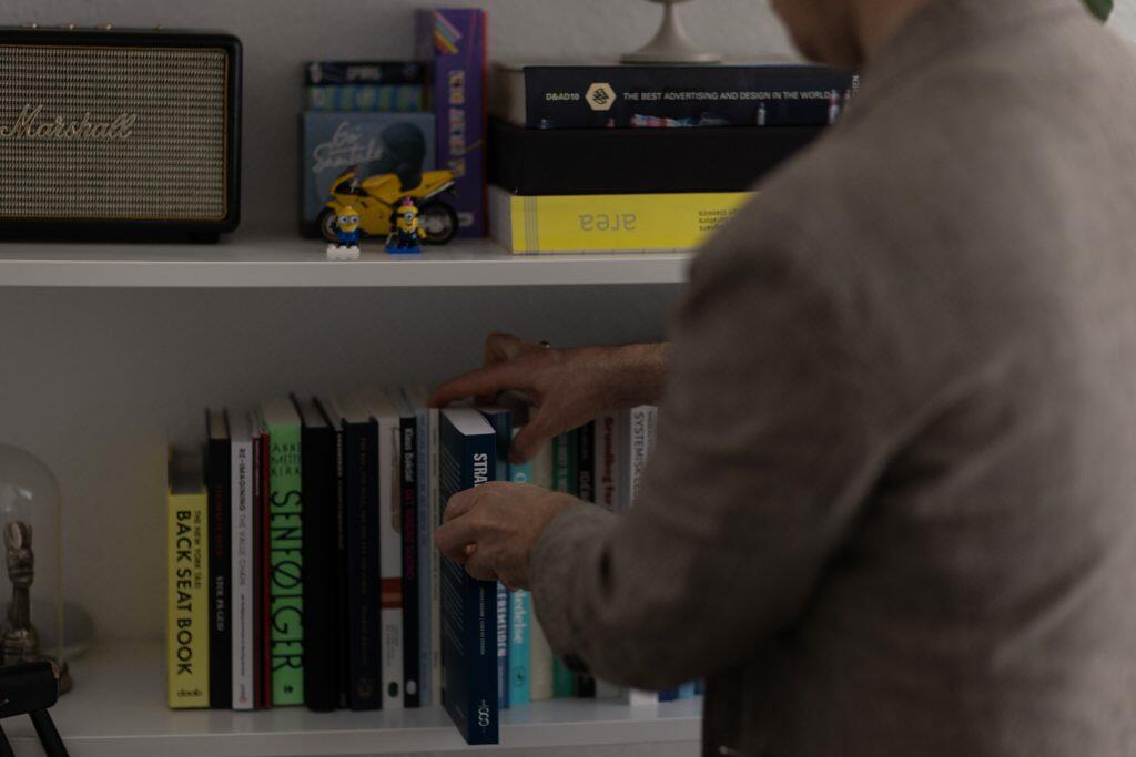 En person arrangerer dygtigt bøger på en hvid bogreol og laver en visuel strategi ved siden af en vintage radio og små figurer.