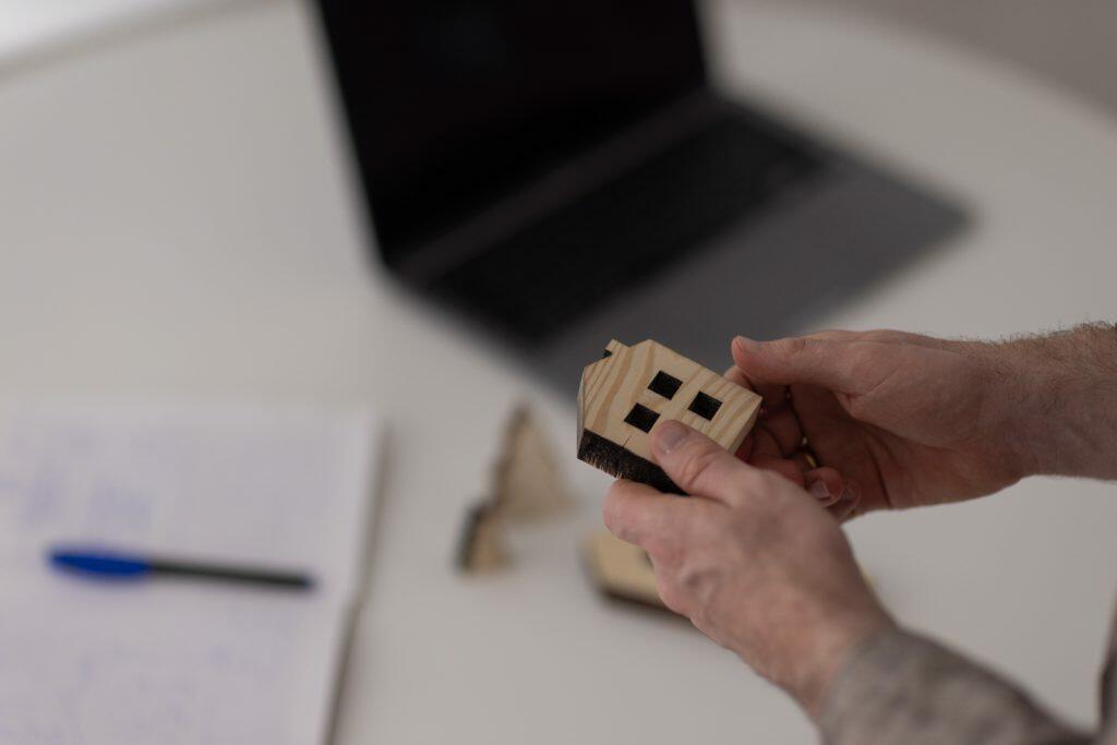 En person holder en lille træhusmodel, der inkarnerer en strategisk vision, mens en bærbar computer og papirer hviler på bordet i baggrunden. Scenen afspejler et billede af tankevækkende branding i aktion.