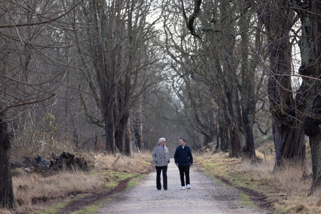 To mennesker, der går langs en trækantet sti, omgivet af bare grene og bladløse træer, skaber et fredfyldt billede af naturens skarpe skønhed. Denne scene kunne tjene som et inspirerende element i strategisk branding-indsats, der understreger ro og sammenhæng med naturen.