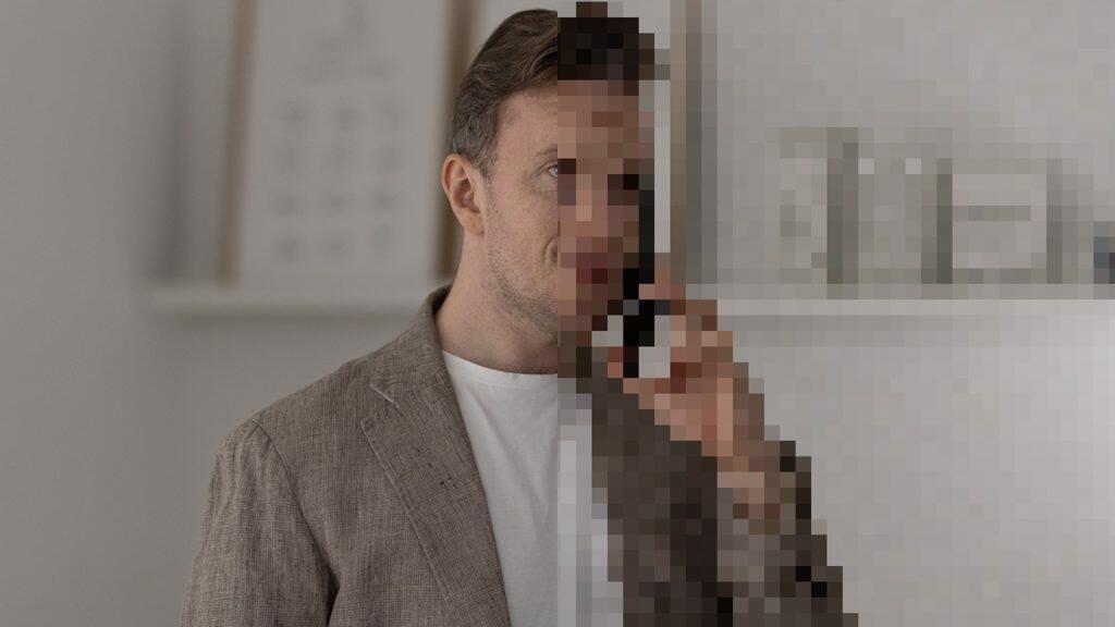 En mand i en grå blazer står, halvdelen af sit billede pixeleret – måske et nik til unikke brandingstrategier. Hylder med varer er synlige i baggrunden.